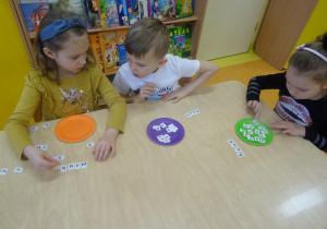 Troje dzieci układa wyraz bank z rozsypanki literowej.